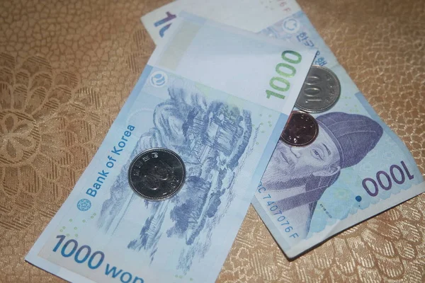 Silver shining Korean won coin scattered over Korean notes on a wooden floor.