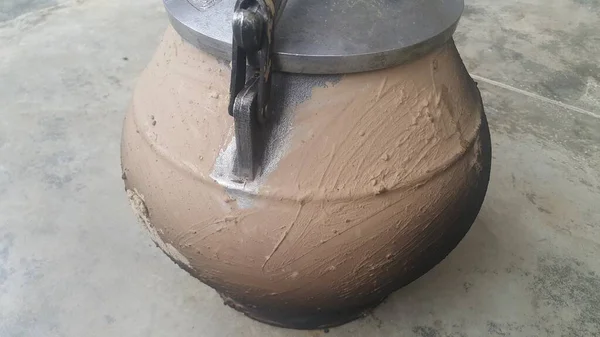 Pressure cooker covered with mud for cooking on fire. Cauldron type rural pressure cooker.