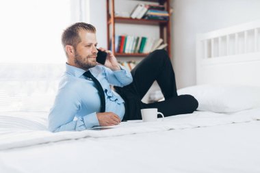 Cep telefonuyla otel odasında çalışan genç bir işadamı.