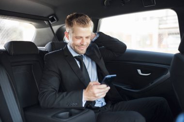 Bir cep telefonu kullanarak araba arkasında oturan çift iş adamı