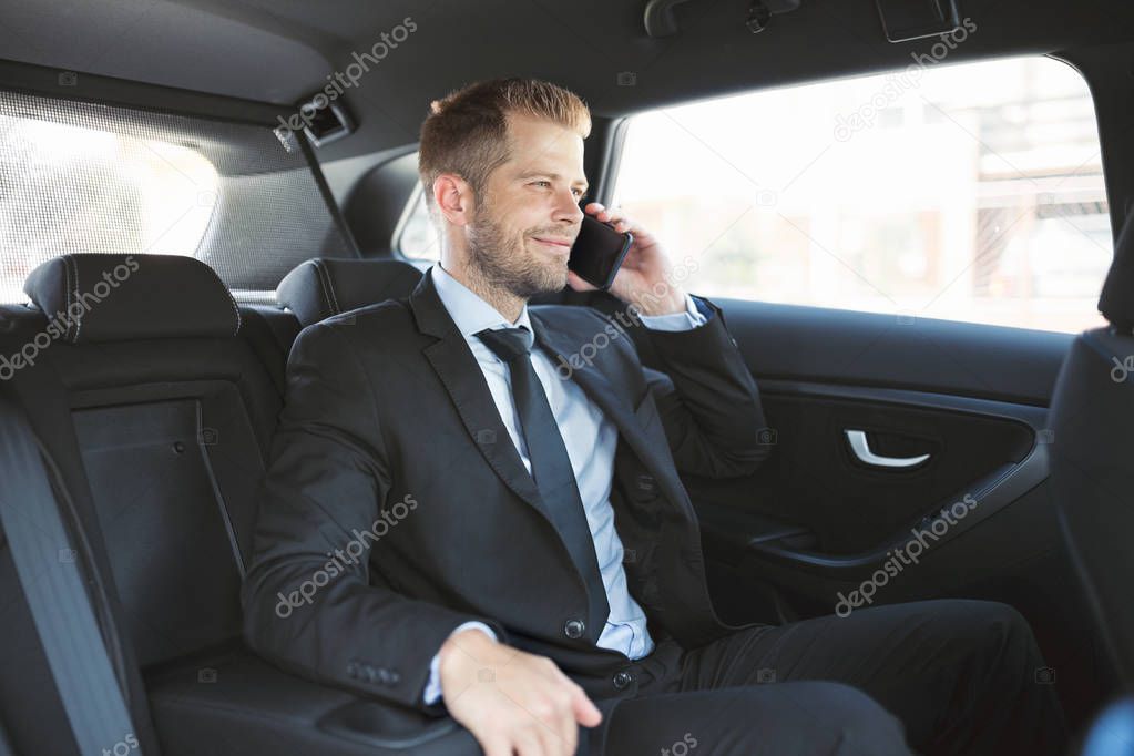 Executive businessman sitting at the back of car using a mobile phone