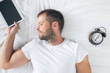 Yorgun bir adam onun dijital tablet kullandıktan sonra yatağa yatıyor