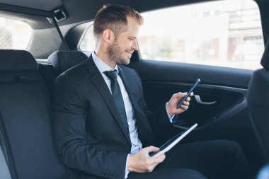 Bir cep telefonu kullanarak araba arkasında oturan çift iş adamı