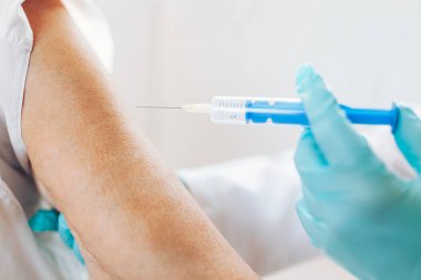 Doktor yaşlı bir hastaya aşı uyguluyor.