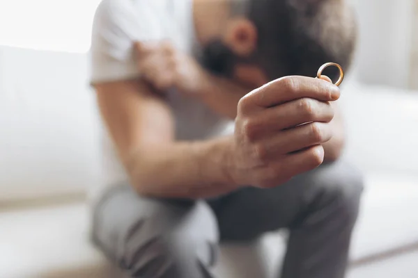 Heartbroken man at home holding a wedding ring