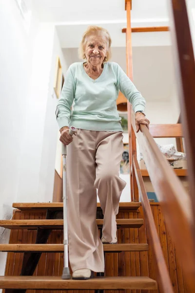 Mujer mayor en casa usando un bastón para bajar las escaleras —  Fotos de Stock