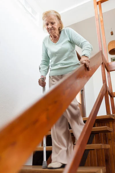 Bejaarde vrouw thuis met behulp van een stok om de trap af — Stockfoto