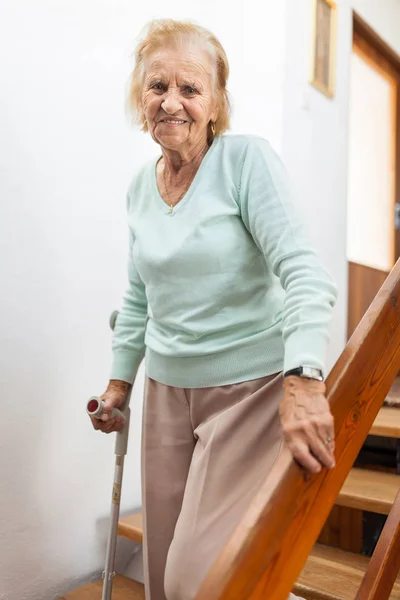 Äldre kvinna hemma med en käpp för att få ner för trapporna — Stockfoto