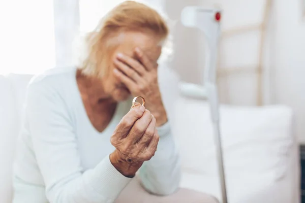 Mujer anciana con el corazón roto sosteniendo un anillo de bodas — Foto de Stock