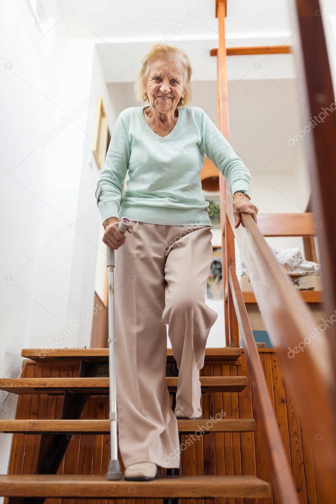 Elderly woman at home using a cane to get down the stairs