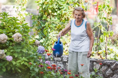 Yaşlı kadın bahçesinde bitkiler sulama