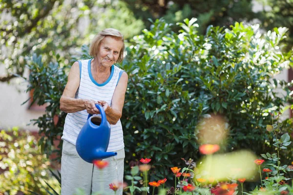 Mulher idosa regando plantas em seu jardim — Fotografia de Stock