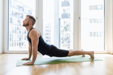 Genç yakışıklı adam evde yoga yapıyor.