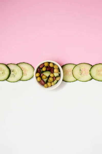 beyaz pembe arka plan üzerinde dilimlenmiş taze salatalık ve salata