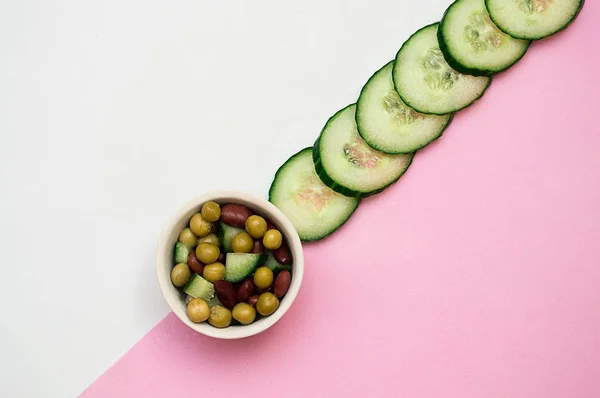 beyaz pembe arka plan üzerinde dilimlenmiş taze salatalık ve salata
