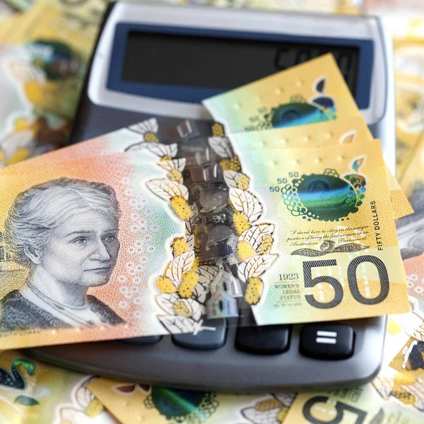 Australian fifty dollar banknote over a calculator. The new 2019 issue bill is designed to deter counterfeiting, the note is polymer and water resistant with a clear holographic strip in a square format.