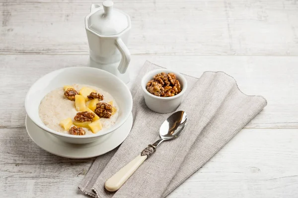 健康的な朝食のクローズ アップ写真 甘いパイナップルとティーポットの灰色の木製テーブルの上の白いプレートにナッツとオートミール — ストック写真