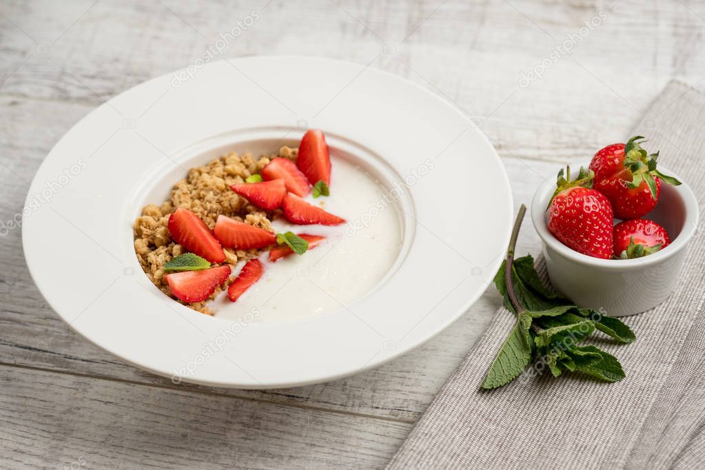 close-up photo of healthy breakfast. Sweet oatmeal with fresh strawberries and green mint leaves in white plate on grey wooden table