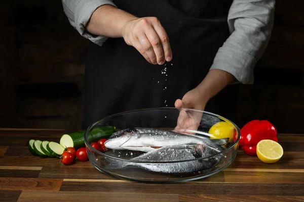 Chef cooking sea fish with citrus and vegetable ingredients on wooden table