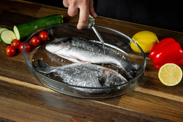 Chef cooking sea fish with citrus and vegetable ingredients on wooden table