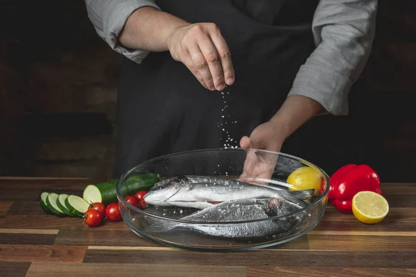 Chef cooking sea fish with citrus and vegetable ingredients on wooden table