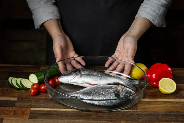 Chef cooking sea fish with citrus and vegetable ingredients on wooden table