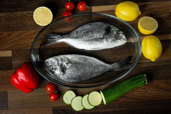 Fresh sea fish with citrus and vegetable ingredients on wooden table.