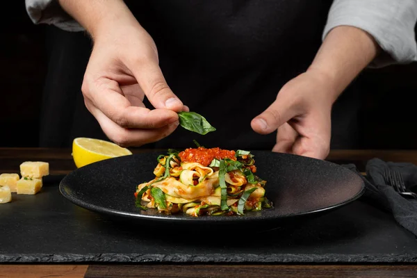 Chef cooking zucchini Italian dish cooking with cheese and tomato sauce, steps on black background kitchen.