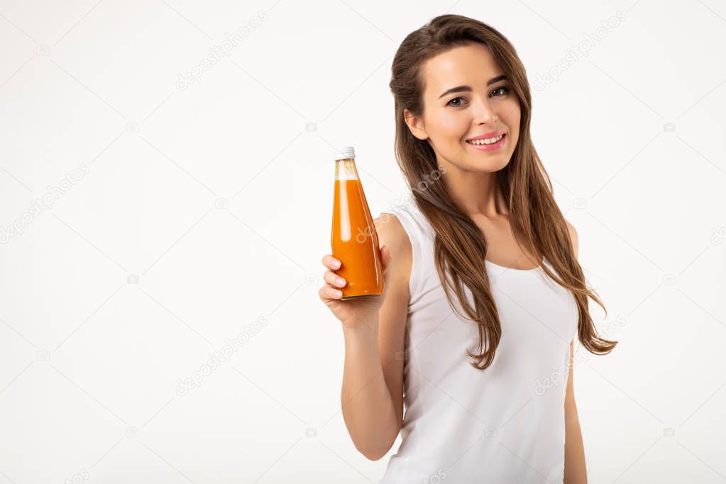 Studio portrait of young woman holding bottle with juice standing on white background