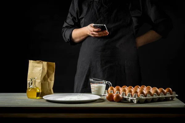 Chef working on dough recipe and holding smartphone. Food concept