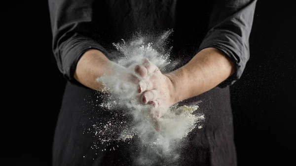 Chef hands sifting flour on black background