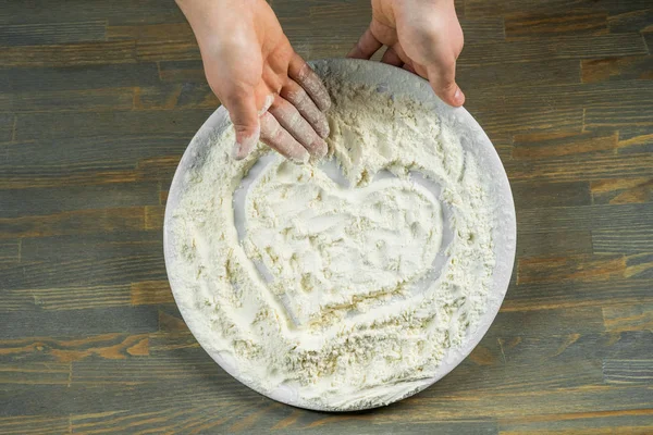 Chef hands making heart in flour over wooden background. Food concept