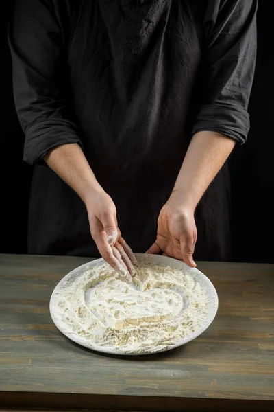 Chef hands making heart in flour over wooden background. Food concept