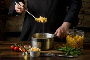 Şef penne makarna bir bölümünü içine kaynar su yakın çekim siyah bir arka plan ile bir tencerede düşürür