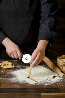 Şef kesme hamur makarna bir oklava, bir kağıt torba ve kıyılmış makarna un ahşap tablo için. Ev yemekleri kavramı