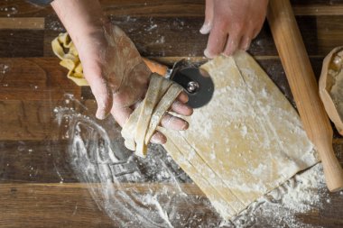 Şef kesme hamur makarna bir oklava, bir kağıt torba ve kıyılmış makarna un ahşap tablo için. Üstten görünüm, ev yemekleri kavramı