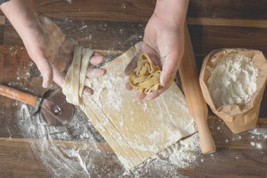 Şef kesme hamur makarna bir oklava, bir kağıt torba ve kıyılmış makarna un ahşap tablo için. Üstten görünüm, ev yemekleri kavramı