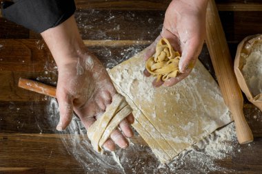 Şef kesme hamur makarna bir oklava, bir kağıt torba ve kıyılmış makarna un ahşap tablo için. Üstten görünüm, ev yemekleri kavramı