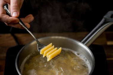 Şef penne makarna bir bölümünü içine kaynar su yakın çekim siyah bir arka plan ile bir tencerede düşürür