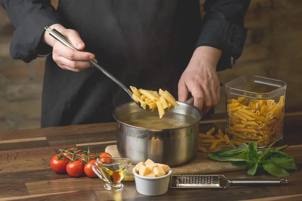 Chef Lowers Portion Penne Pasta Saucepan Boiling Water Close Black — Stock Photo, Image