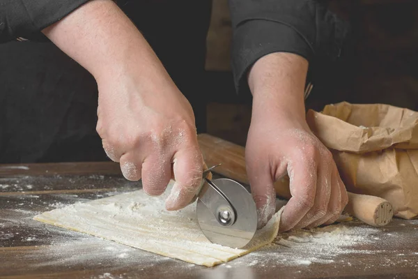 Şef kesme hamur makarna bir oklava, bir kağıt torba ve kıyılmış makarna un ahşap tablo için. Üstten görünüm, ev yemekleri kavramı