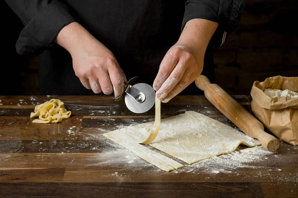 Şef kesme hamur makarna bir oklava, bir kağıt torba ve kıyılmış makarna un ahşap tablo için. Ev yemekleri kavramı