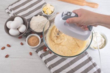 Chef malzemeler mutfak masasında yemeklerle tatlı cheesecake yemek elinde karıştırıcılı