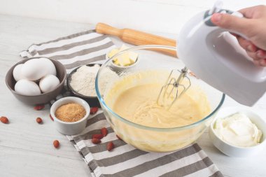 Chef malzemeler mutfak masasında yemeklerle tatlı cheesecake yemek elinde karıştırıcılı
