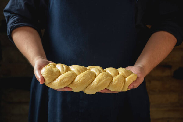 Male baker holding loaf of raw challah jewish bread