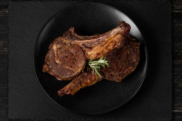 Close view of grilled beef ribs on black plate over wooden background