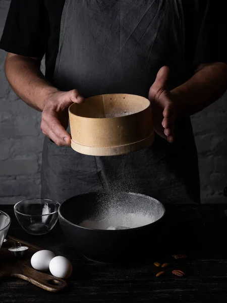 Man bolting flour in black bowl and making dough for pancakes