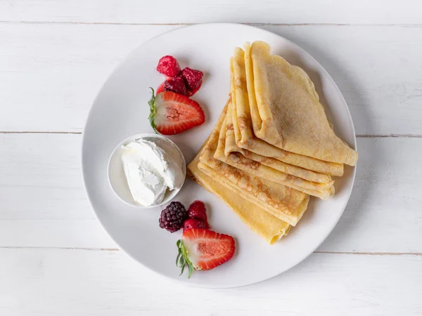 Fresh crepes with ice-cream and berries on white plate on wooden background