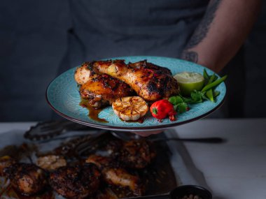 Bir tabak taze pişmiş baharatlı tavuk budu ile tutan adam Görünümü Kapat sarımsak, biber biber, limon dilimi ve otlar ile hizmet 