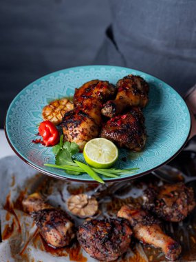 Bir tabak taze pişmiş baharatlı tavuk budu ile tutan adam Görünümü Kapat sarımsak, biber biber, limon dilimi ve otlar ile hizmet 